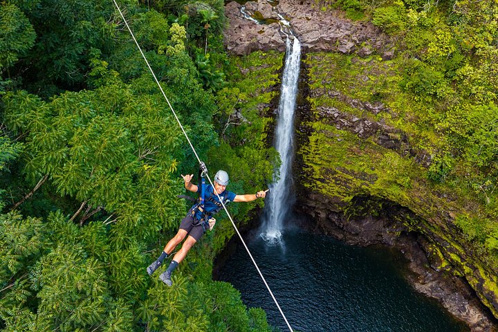 Two riders on a zipline beside a waterfall